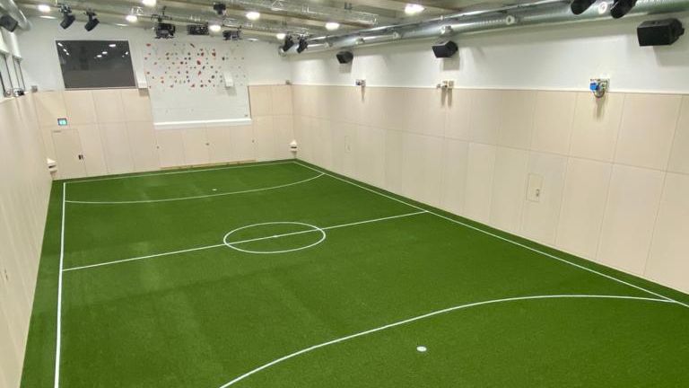Eine Aufnahme eines Indoor-Fußballplatzes bei normalem Licht und ohne Projektionen an der Wand - man erkennt die vielen Kameras und Geräte der Skills.lab Technologie an Decke und Wänden.